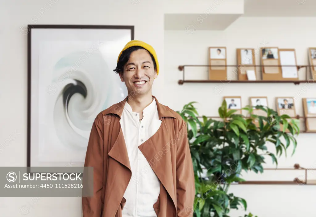 Male Japanese professional standing in a co-working space, smiling at camera.