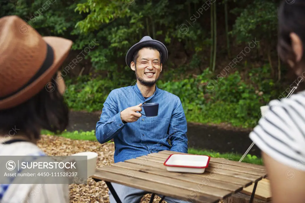 Japanese man and two women sitting outdoors at a table, drinking coffee.