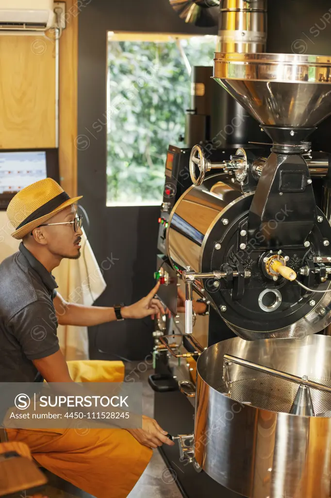 Japanese man wearing hat and glasses sitting in an Eco Cafe, operating coffee roaster machine.
