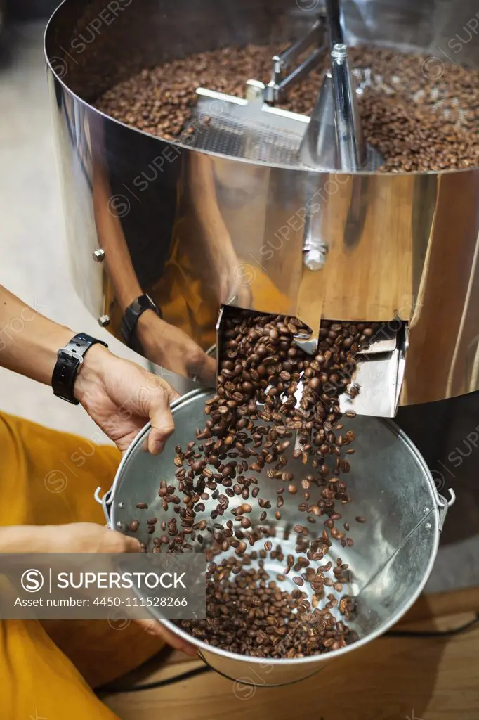 High angle close up of person holding metal bucket with freshly roasted coffee beans.