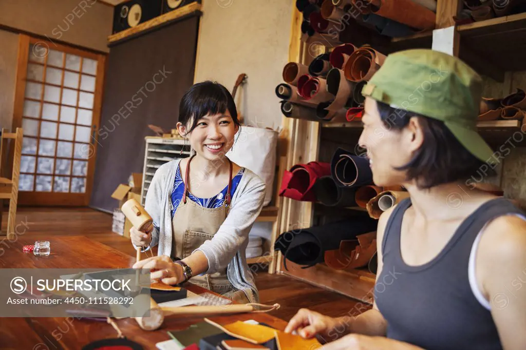 Two Japanese women sitting at a table, working in a leather shop.