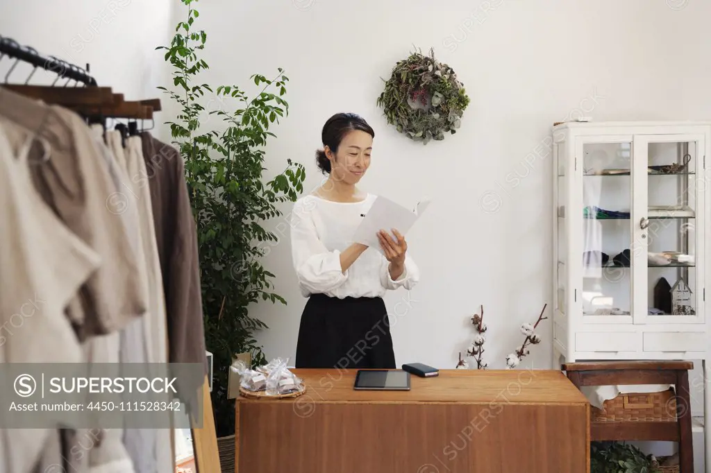 Japanese woman standing in a small fashion boutique, reading brochure.