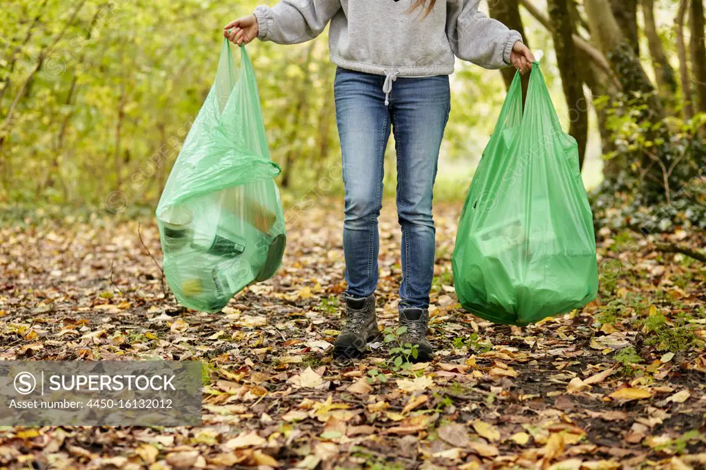 Woman walking in woodland holding two plastic bags full of rubbish