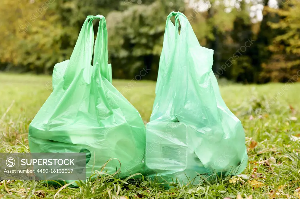 Two full plastic bags sitting side by side on the grass filled with rubbish for recycling