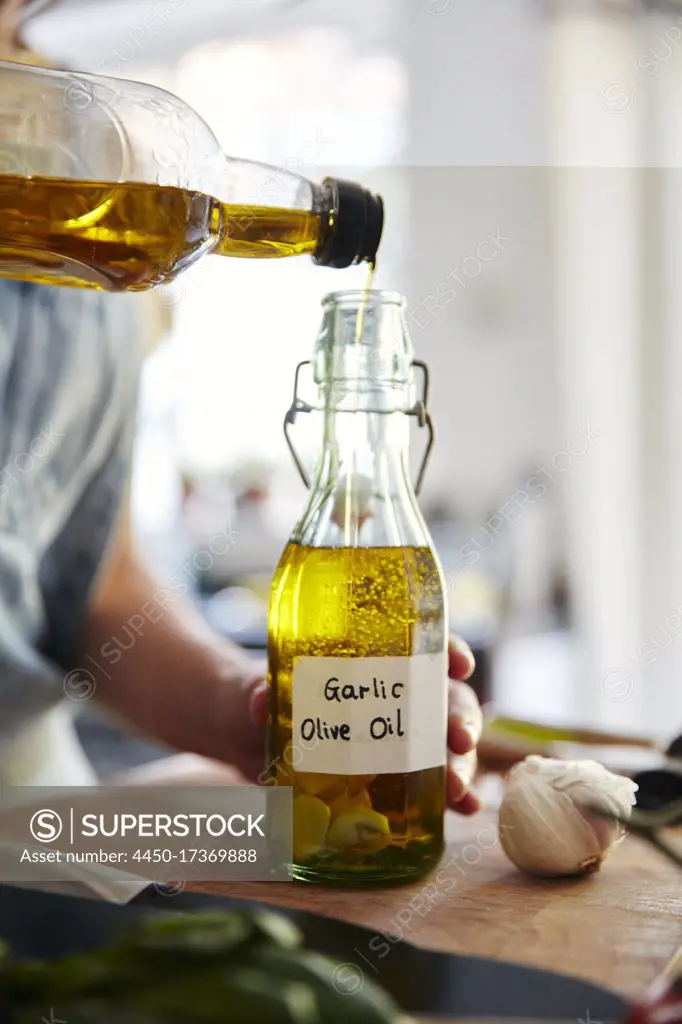 Woman pouring olive oil into bottle containing garlic