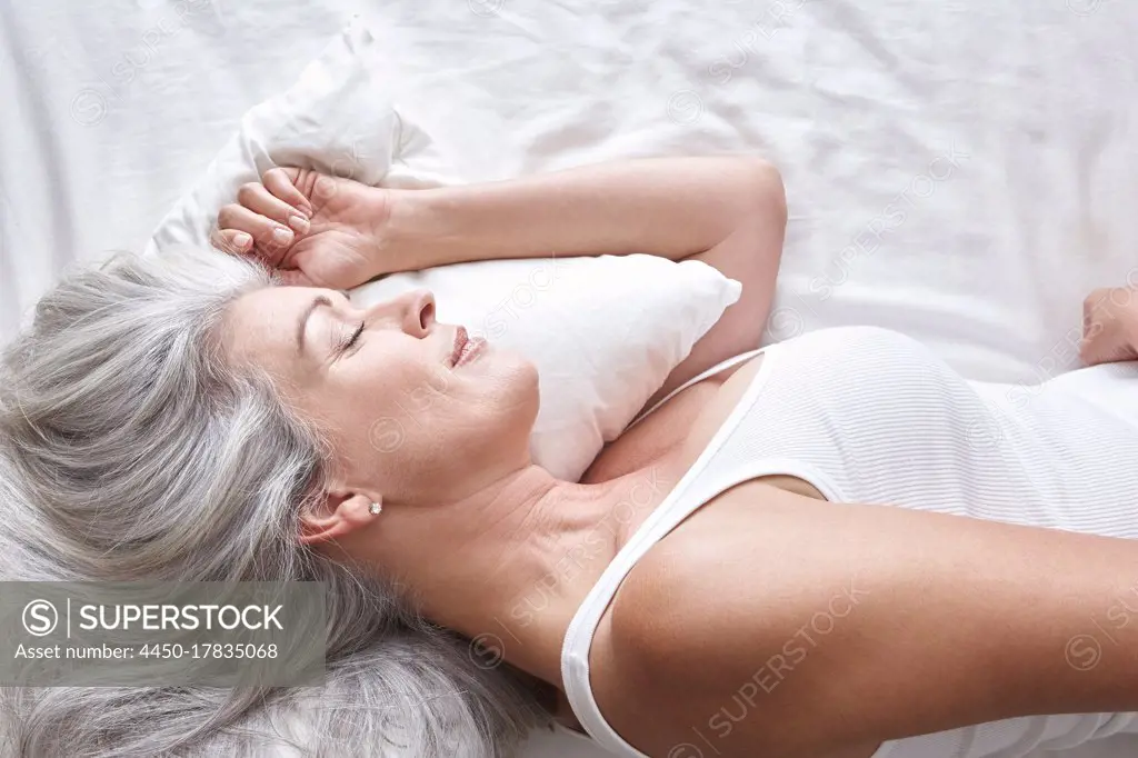 Mature attractive Caucasian woman sleeping on white sheets