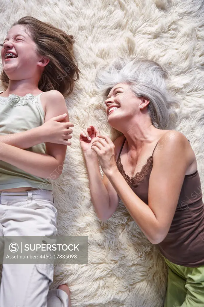 Mature woman and a teenager, mother and daughter lying on the floor laughing
