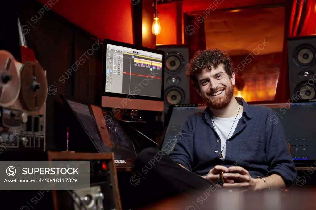 Portrait of man smiling, sitting in music studio holding cup of coffee