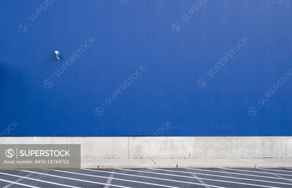 Surveillance camera on a blue exterior wall of warehouse or large windowless building.