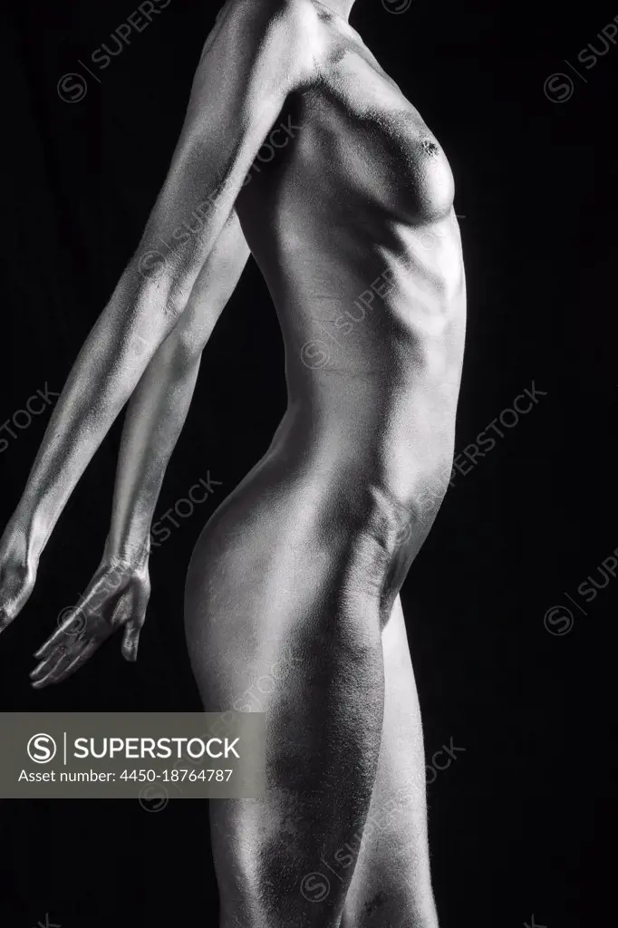 Nude Caucasian woman with silver body paint standing, side view