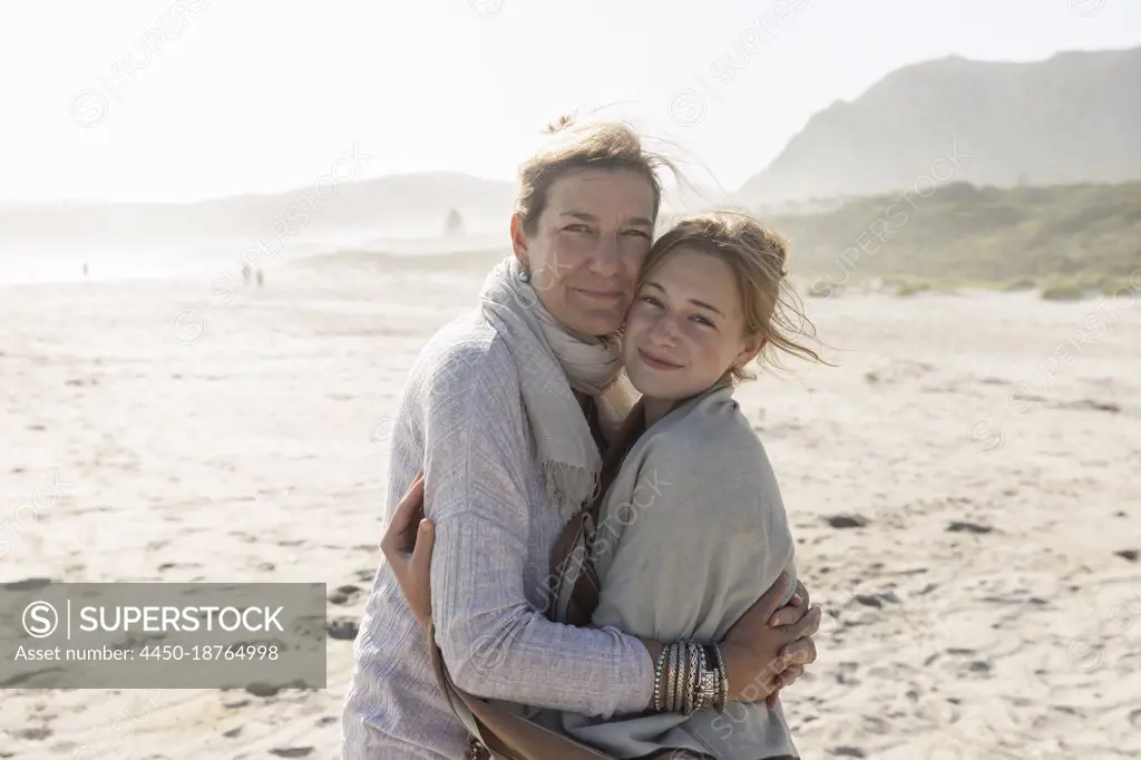 Adult woman and her teenage daughter hugging, standing on a windswept beach