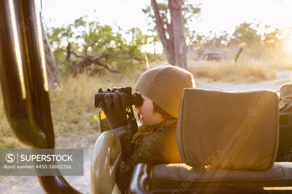 Young boy in a jeep using binoculars, a dawn drive through the bush. 