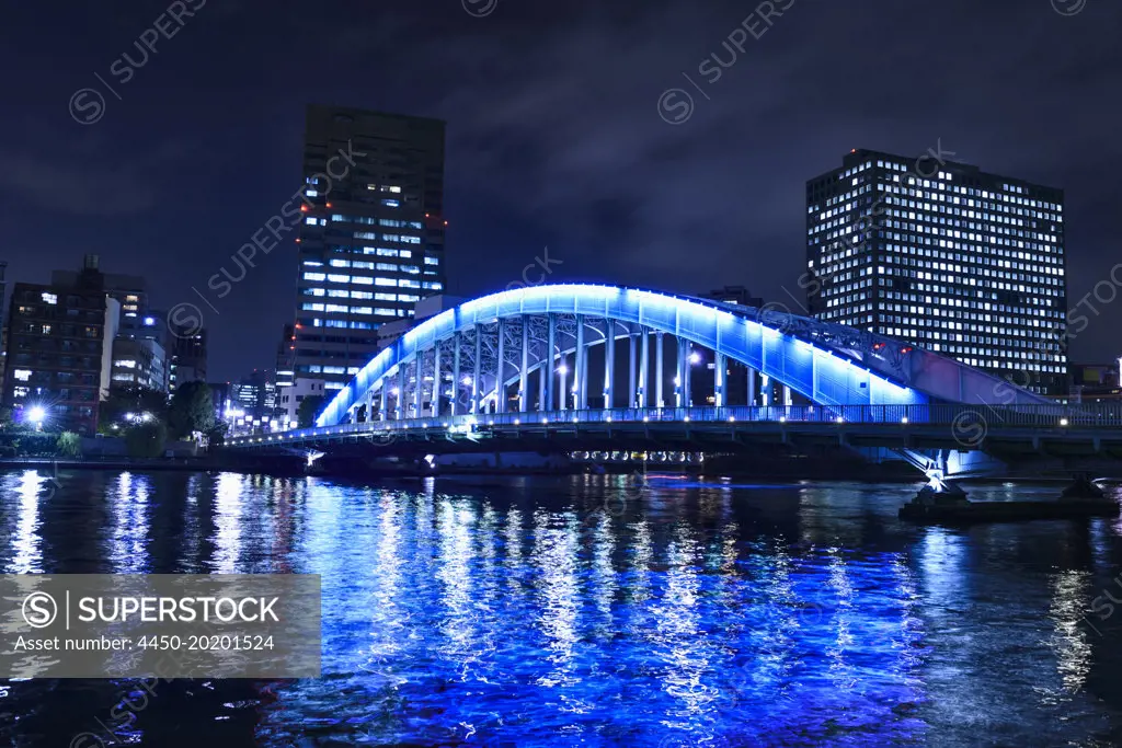 The city of Tokyo at night, the Sumida River and Eitai bridge, lit up, with high rise buildings. 
