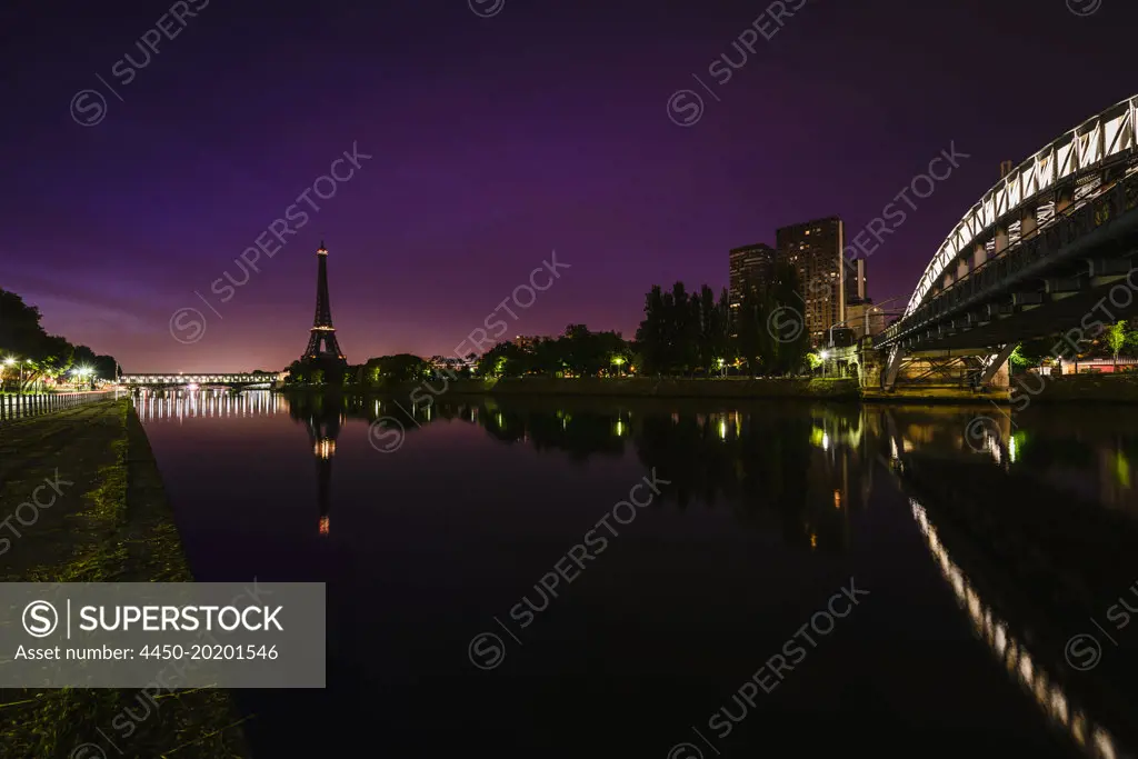 A view along the water of the River Seine at night, tall buildings on the river bank, the Eiffel tower in the distance. 
