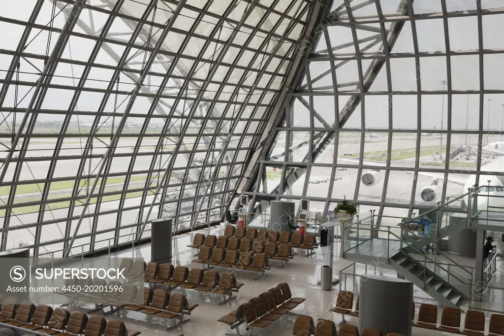 Gate and seats at Bangkok Airport with airplanes viewed through the glass windows and walls.