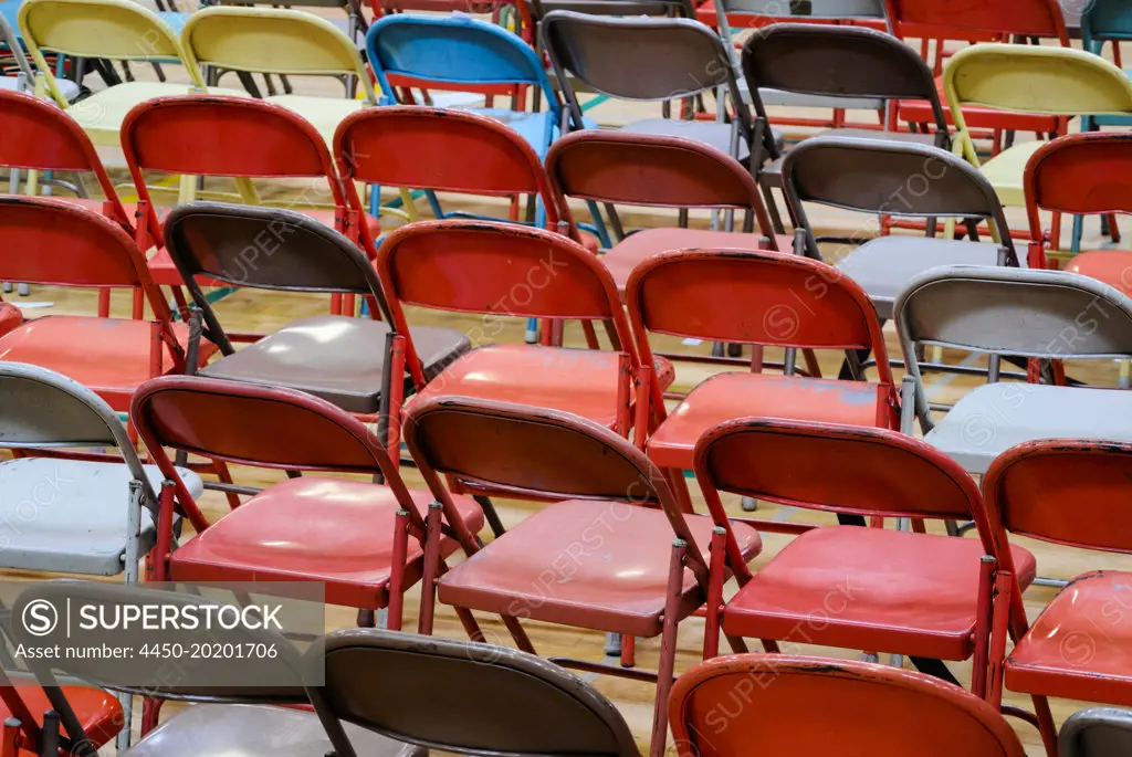 Rows of metal folding chairs of different colours, grey, red, yellow. 