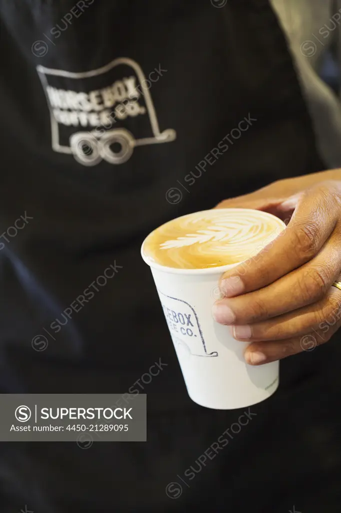 Close up of woman holding coffee in a paper cup.