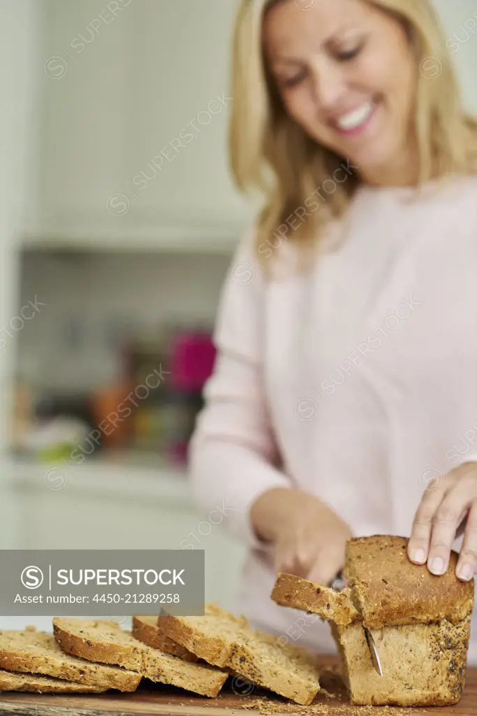 A woman slicing a loaf of brown bread.