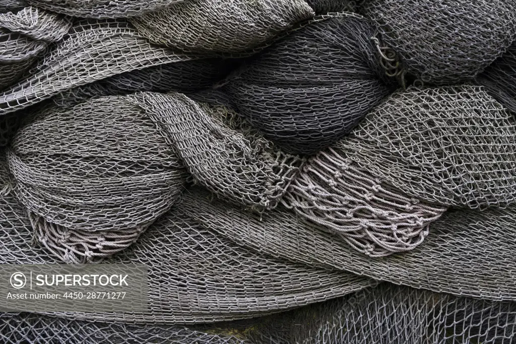 A heap or pile of commercial fishing nets, grey netting folded up. -  SuperStock