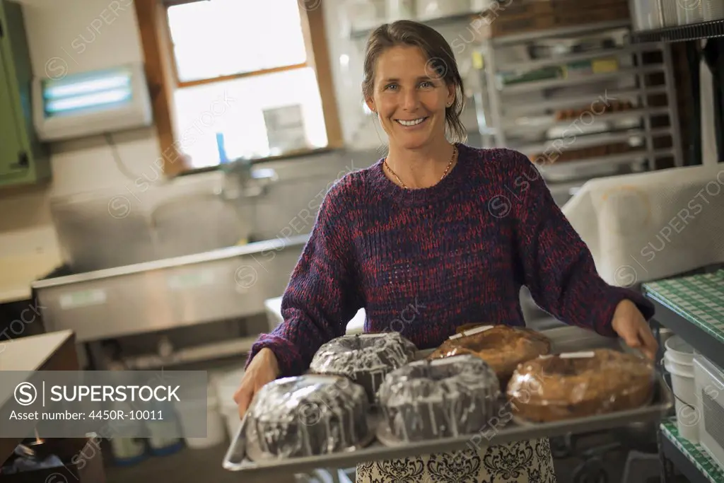 A woman in a kitchen carrying a tray of iced fresh baked cakes. Accord, New York, USA