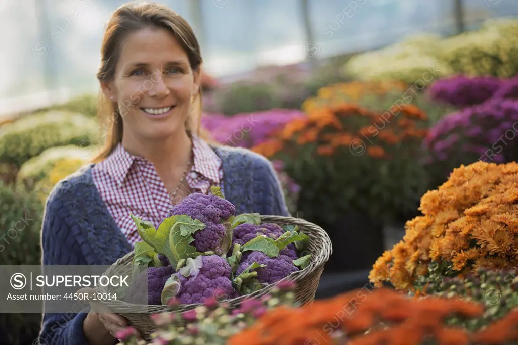 A woman holding a bowl of fresh produce, purple sprouting broccoli. Flowering plants. Crysanthemums.Woodstock, New York, USA