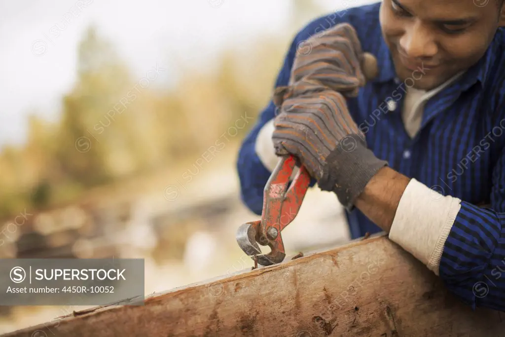 A man working in a reclaimed timber yard. Using a tool to remove metals from a reclaimed piece of timber. Pine Plains, New York, USA