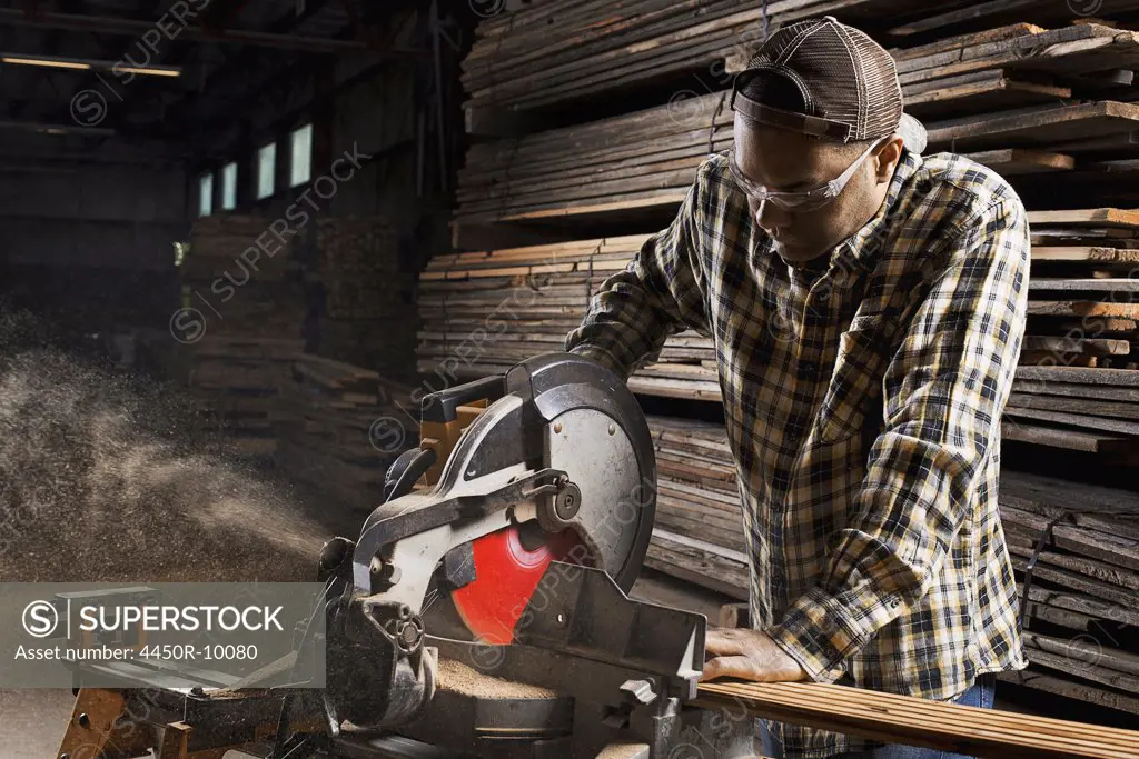 A reclaimed lumber workshop. A man in protective eye goggles using a circular saw to cut timber. Woodstock, New York, USA