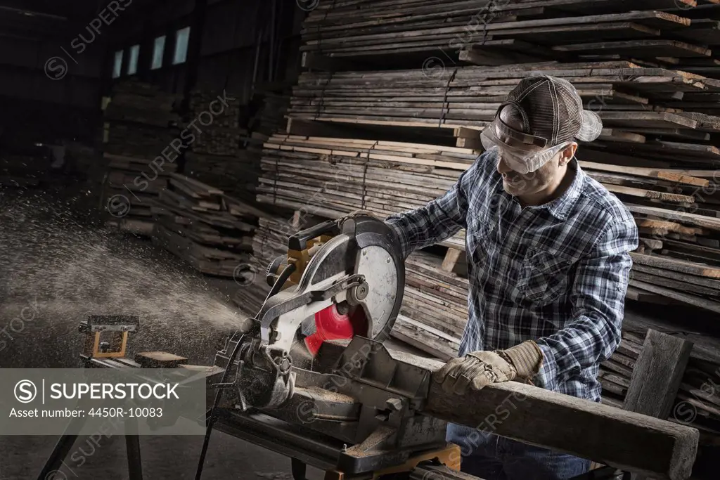 A reclaimed lumber workshop. A man in protective eye goggles using a circular saw to cut timber. Woodstock, New York, USA