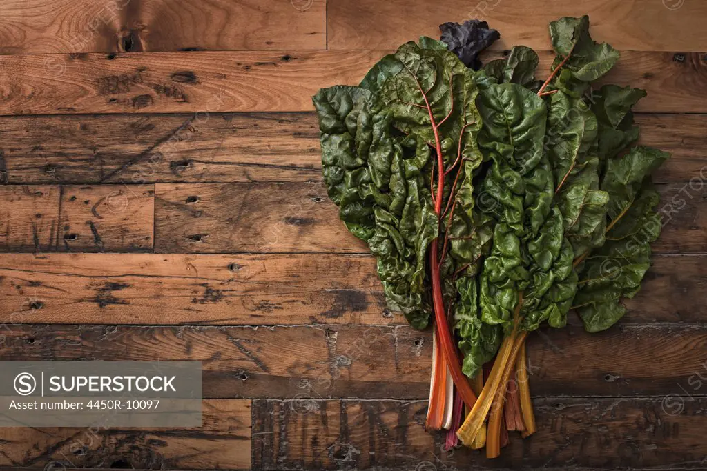 A group of red and orange chard leaves with bright coloured stems. Organic vegetables, frehsly picked, and placed on a wooden board. Woodstock, New York, USA