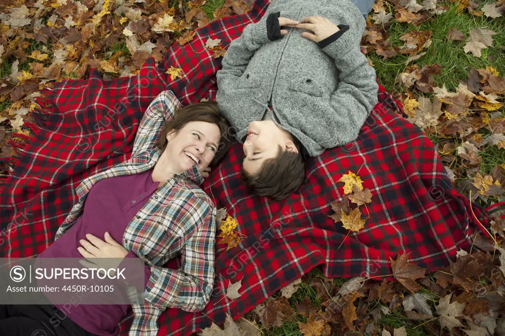 Two people, a woman and a child, lying on a red tartan picnic blanket, looking upwards. Woodstock, New York, USA