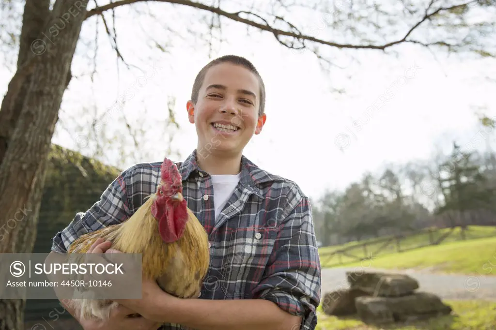 An animal sanctuary. A young boy holding a chicken with brown feathers and a red coxcomb.Saugerties, New York, USA