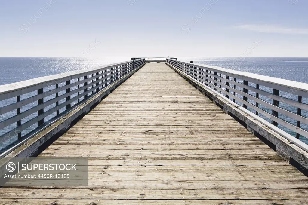 A long pier with railings extending out over the Pacific Ocean leading to the horizon.San Luis Obisbo County, California, USA