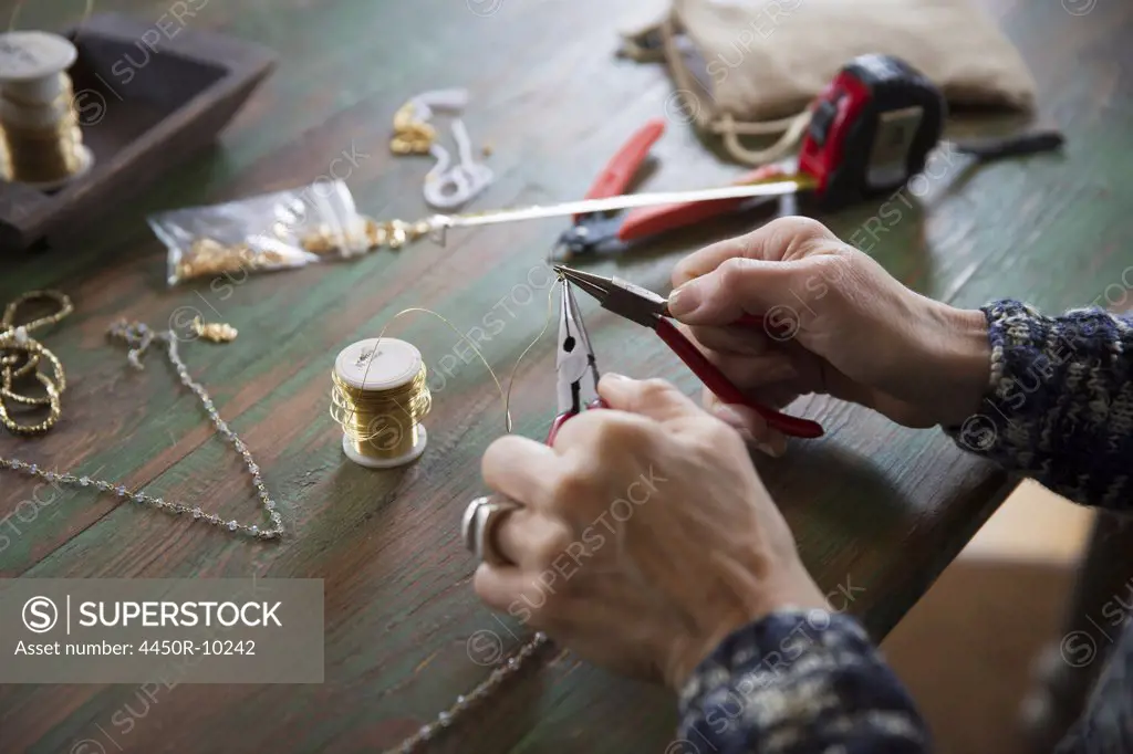 A tabletop with jewellery making equipment. Hands twisting wire on a necklace. New York, USA