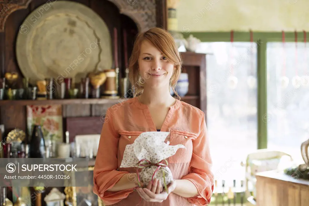 A young woman standing in a store full of antique objects, holding a tied packet with ribbon. New York, USA