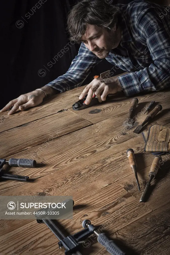 A man working in a reclaimed lumber yard workshop. Holding tools and sanding knotted and uneven piece of wood. Pine Plains, New York, USA