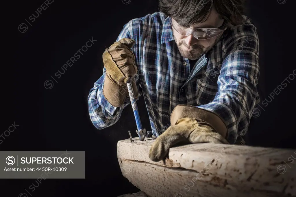 A man working in a reclaimed lumber yard workshop. Holding tools and extracting nails from a knotted and uneven piece of wood. Pine Plains, New York, USA
