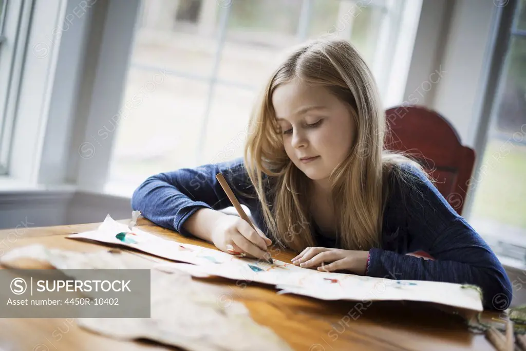 A family home. A young girl sitting at a table drawing on a large piece of paper. Holding a pencil. Woodland Valley, New York, USA