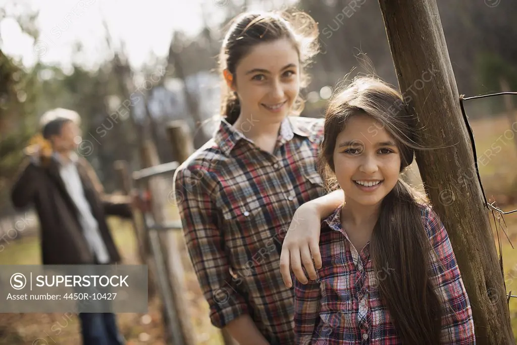 Two young girls beside a paddock fence, and a man in the background. An organic farm.Woodstock, New York, USA