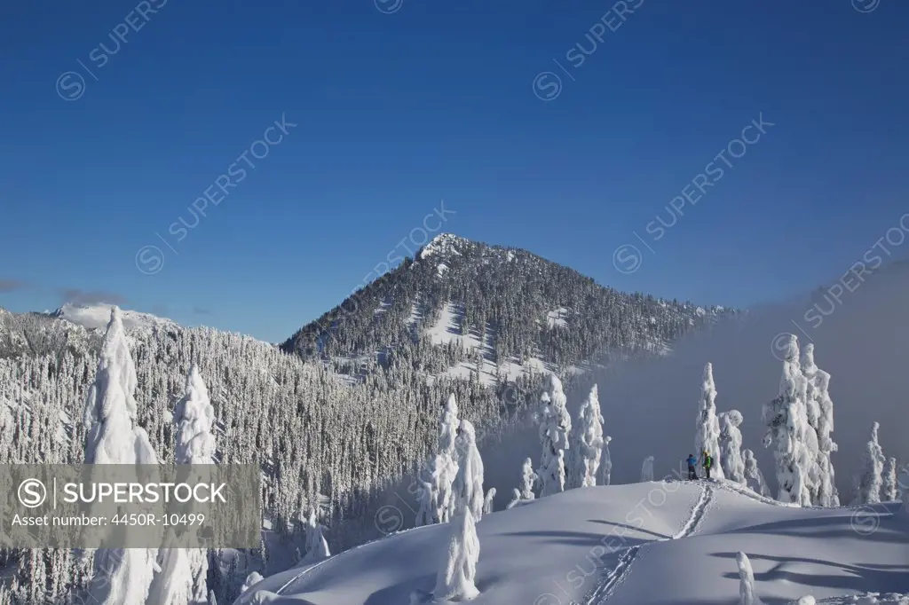 Two hikers enjoy a blue bird day in the middle of winter in the snow covered Cascade Mountains.Cascade Mountains, Washington, USA