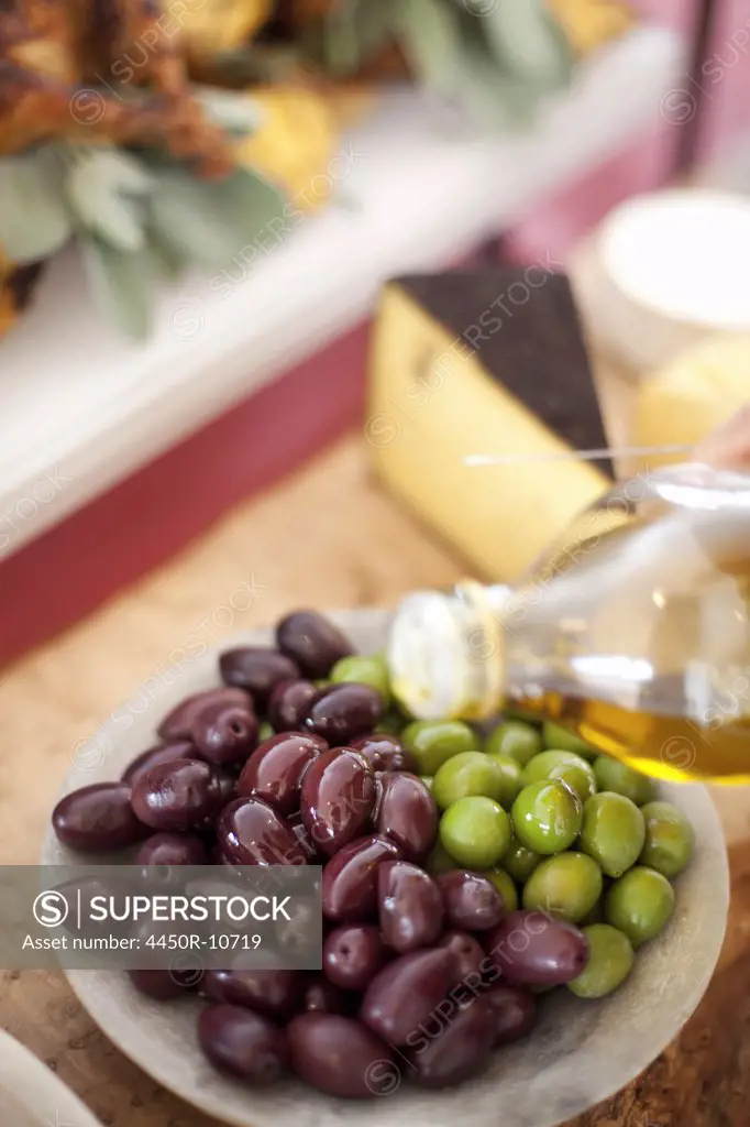 A dish of fresh organic vegetables. Green and black olives on a plate with a drizzling of olive oil from a bottle. Prepared farmstand foods for a party Salt Lake City, Utah, USA