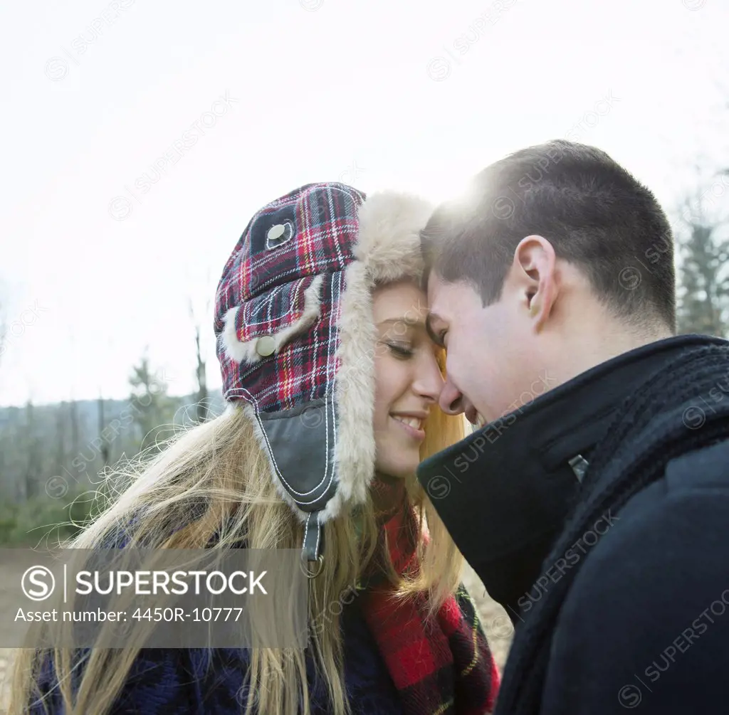 A couple, young man and woman, face to face embracing, outdoors on a cold winter day.  Woodstock, New York, USA