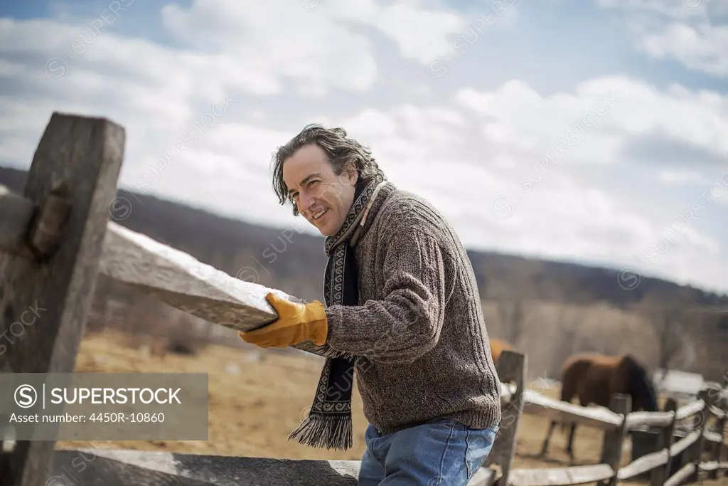 A man fixing a post and rail fence around a horse paddock. Cold Spring, New York, USA