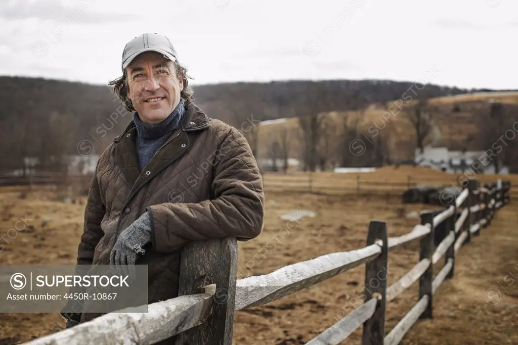 A man leaning against a post and rail fence on a farm in winter. Cold Spring, New York, USA