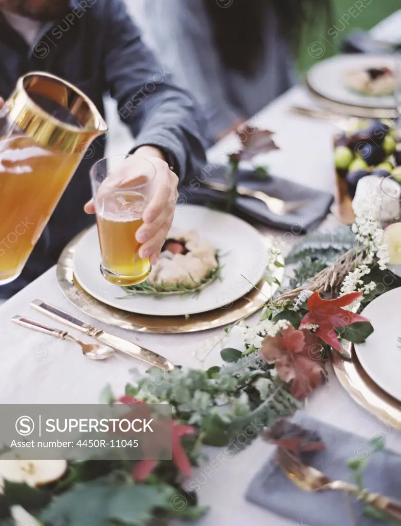 A group of people around a table in a garden. A celebration meal, with table settings and leafy decorations. A person pouring drinks into glasses. Provo, Utah, USA