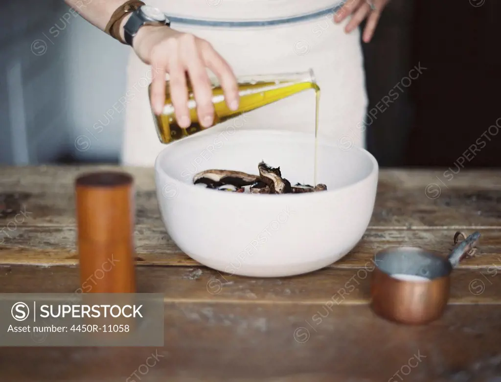 A domestic kitchen. A woman wearing an apron, dressing a fresh salad of vegetables in a bowl with oil.  Provo, Utah, USA