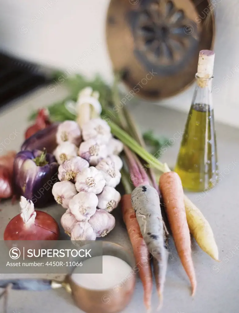 A tabletop. A group of fresh organic vegetables, carrots and onions, garlic and peppers. A flask of oil, and a copper pan of sauce.  Provo, Utah, USA