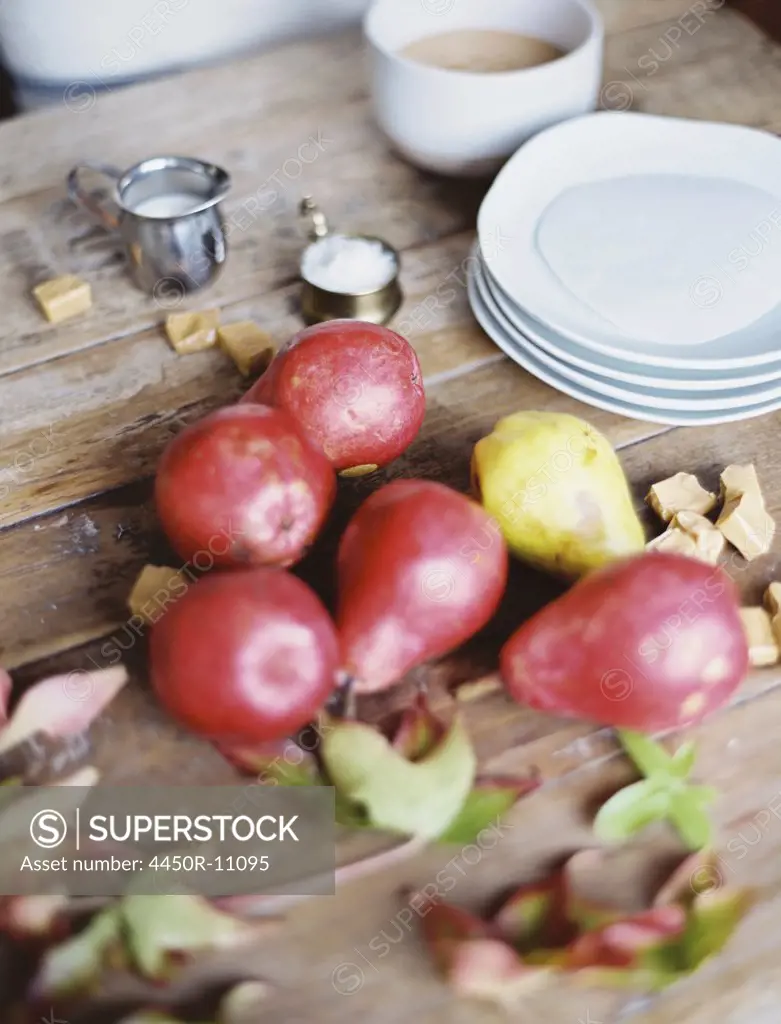 A domestic kitchen tabletop. A small group of fresh organic pears and a stack of white plates.   Provo, Utah, USA
