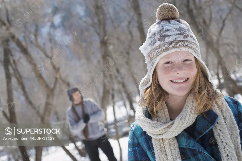 Winter scenery with snow on the ground. A young girl with a bobble hat and scarf outdoors. A man in the background.  Provo, Utah, USA