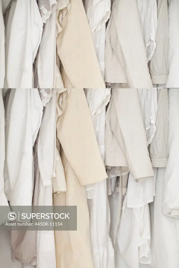 A closet with cream and white clothes, jackets, shirts and tunics hanging up. A row of women's shoes arranged neatly on the floor. Rome, Italy