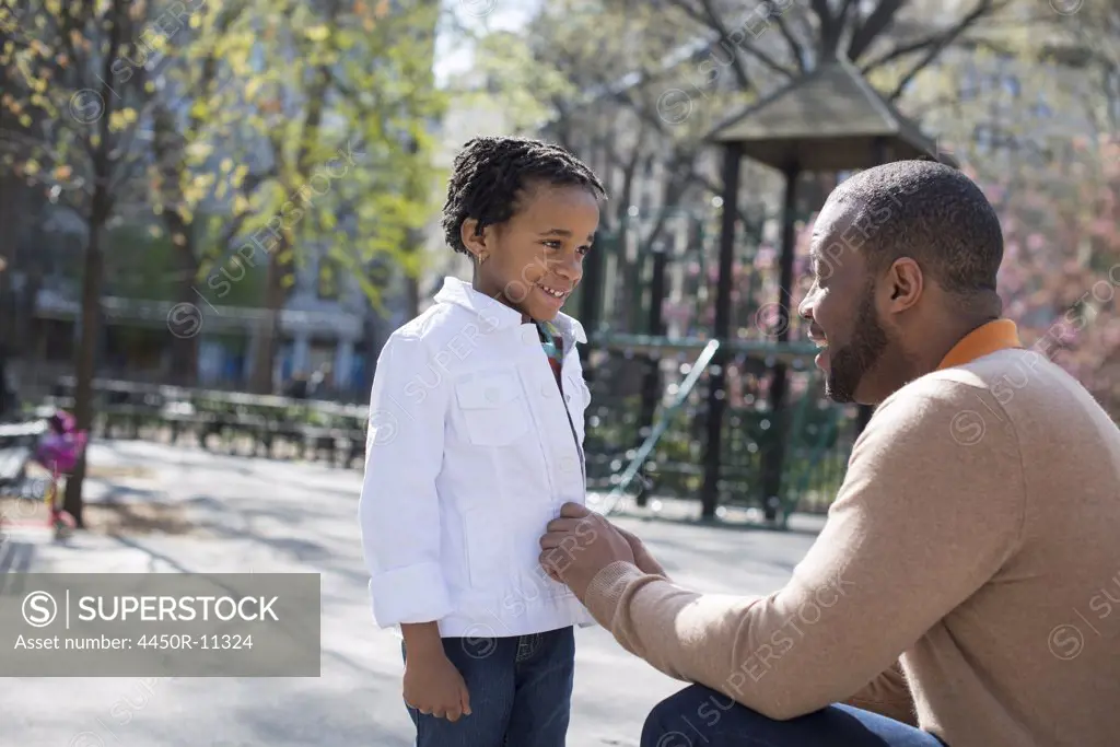 A New York city park in the spring. Sunshine and cherry blossom. A father kneeling and buttoning his son's jacket. New York city, USA